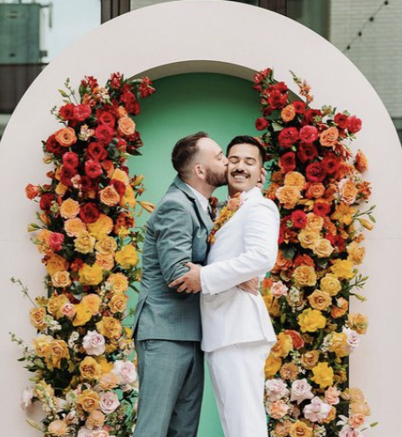 Two grooms in mint green and white suits under circular floral arch