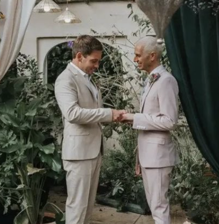 Two grooms in light colored suits shaking hands in garden