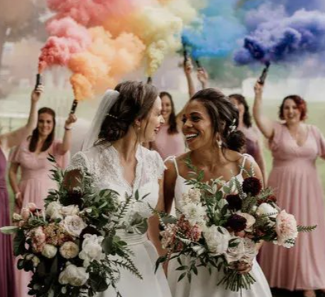 Two brides with colorful smoke and bridesmaids in pink
